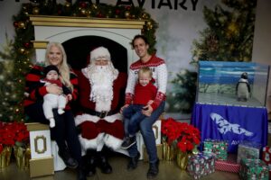 A mom, dad, and two small children sitting next to Santa and his African Penguin friend!