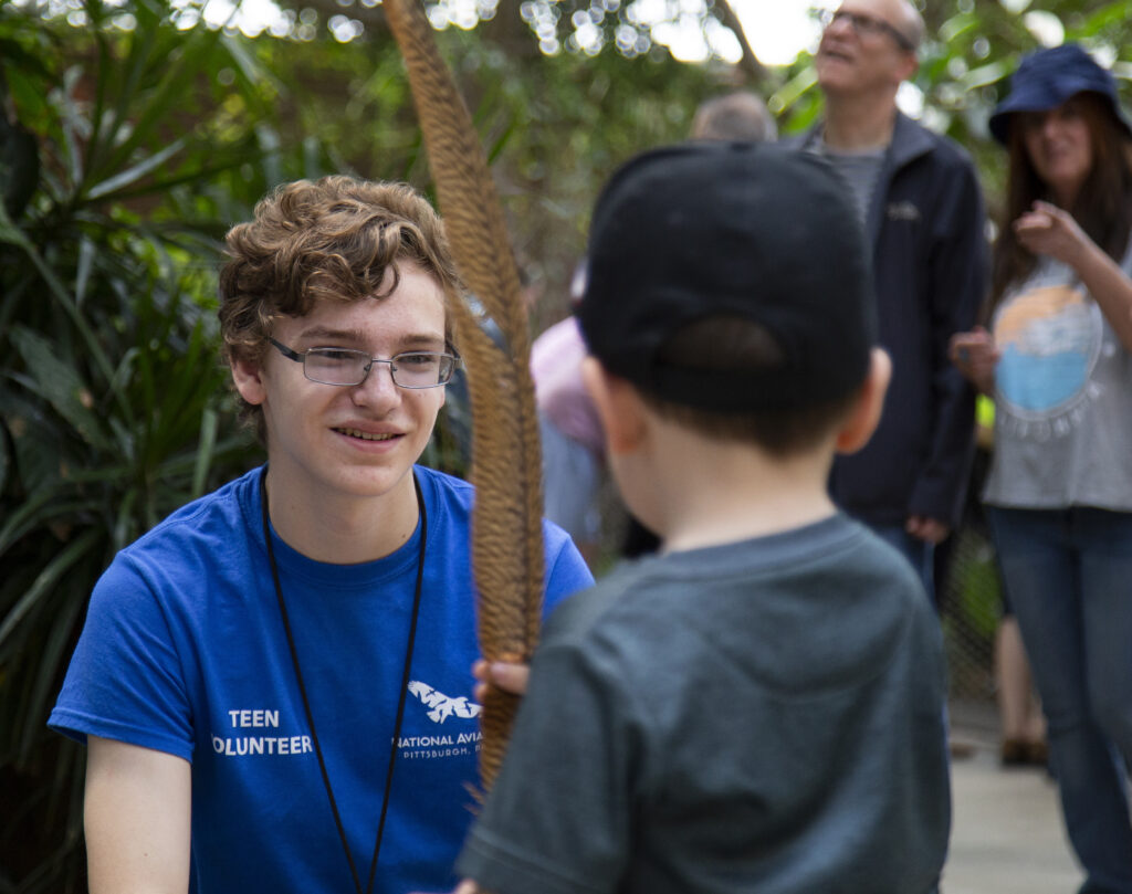 National Aviary Teen Volunteer holding a feather for visitors.