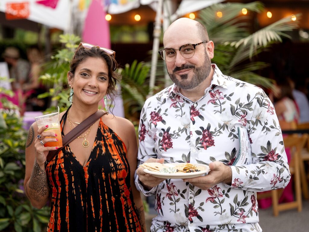 Two guests posing for a photo holding a cocktail and light bites at the National Aviary's Night in the Tropics