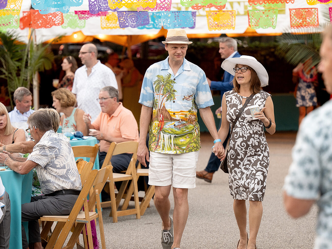 Two guests holding hands walking under papel picado at the National Aviary's Night in the Tropics