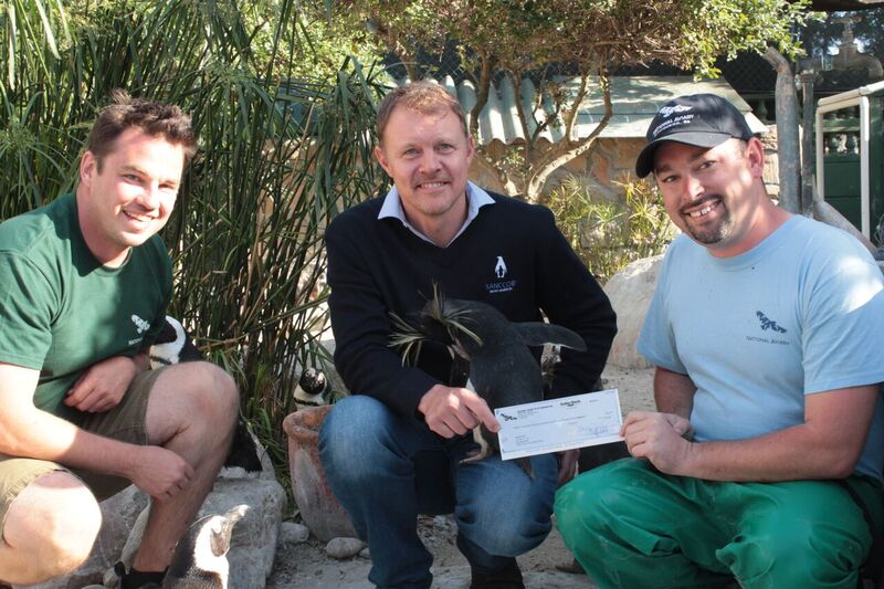 Senior-Education-Trainer-and-Safety-Specialist-Jamie-Travitzleft-and-Assistant-Manager-of-Animal-Care-Chris-Gausright-presenting-a-check-to-SANCCOB-in-South-Africa